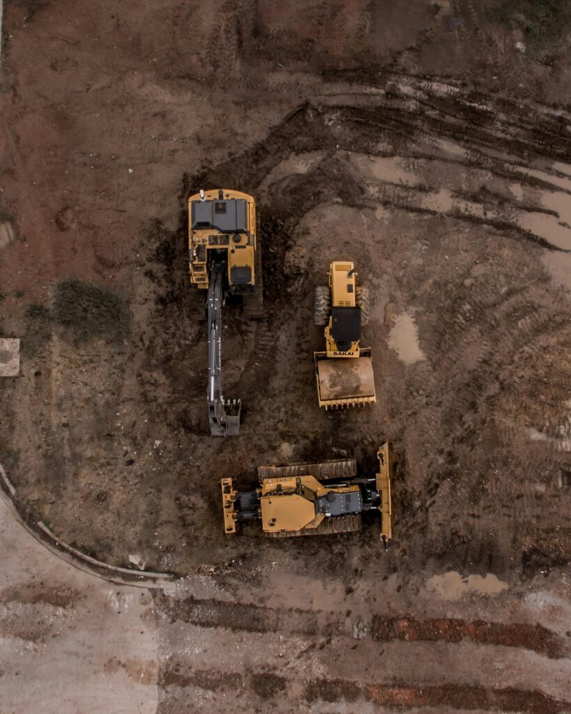 An aerial shot of heavy machinery at a construction site, including excavators and road rollers.