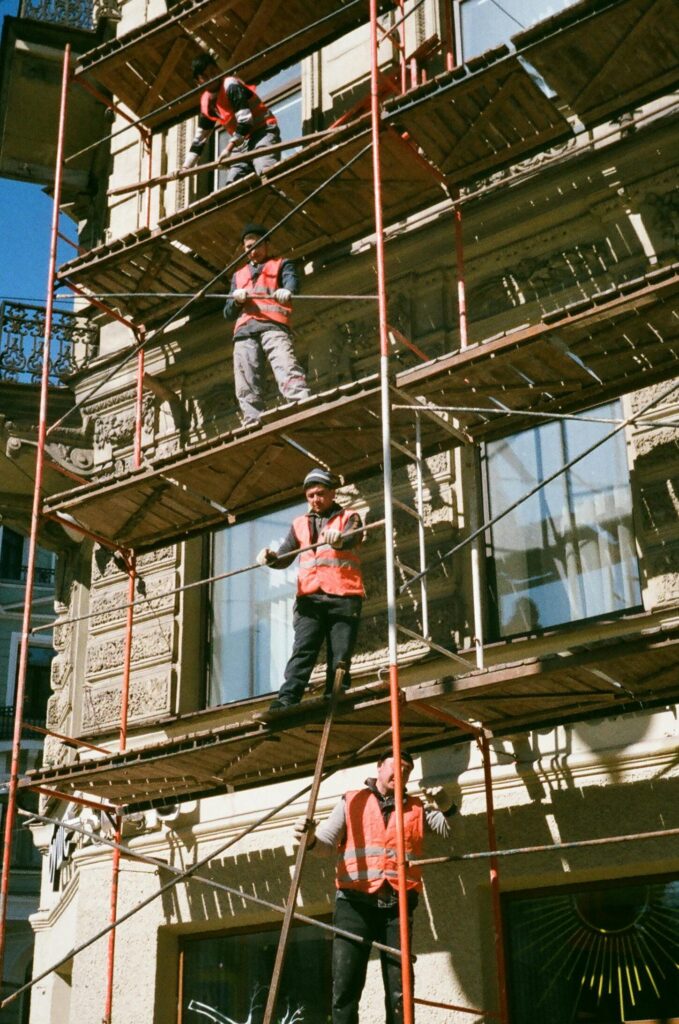 Construction workers on scaffolding renovating a building facade on a sunny day.