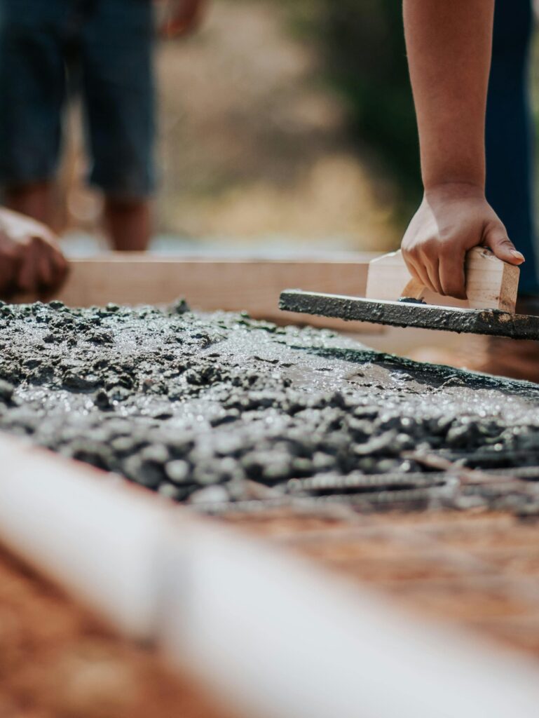 Construction workers leveling fresh cement on a sunny day at an outdoor site.