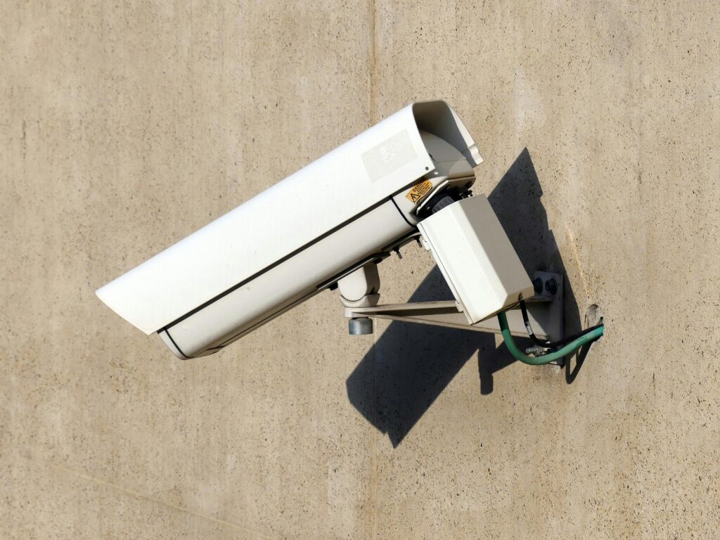 Close-up of a white security camera mounted on a beige wall in sunlight, emphasizing safety.